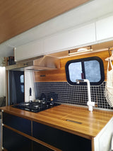 Modern RV rental kitchen with wood-patterned counters, black & white tiles, and essential appliances for comfortable travel.