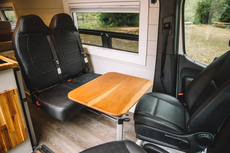 RV rental interior: A cozy dining area with two rear passenger seats, a wooden table, and a swiveled front seat.