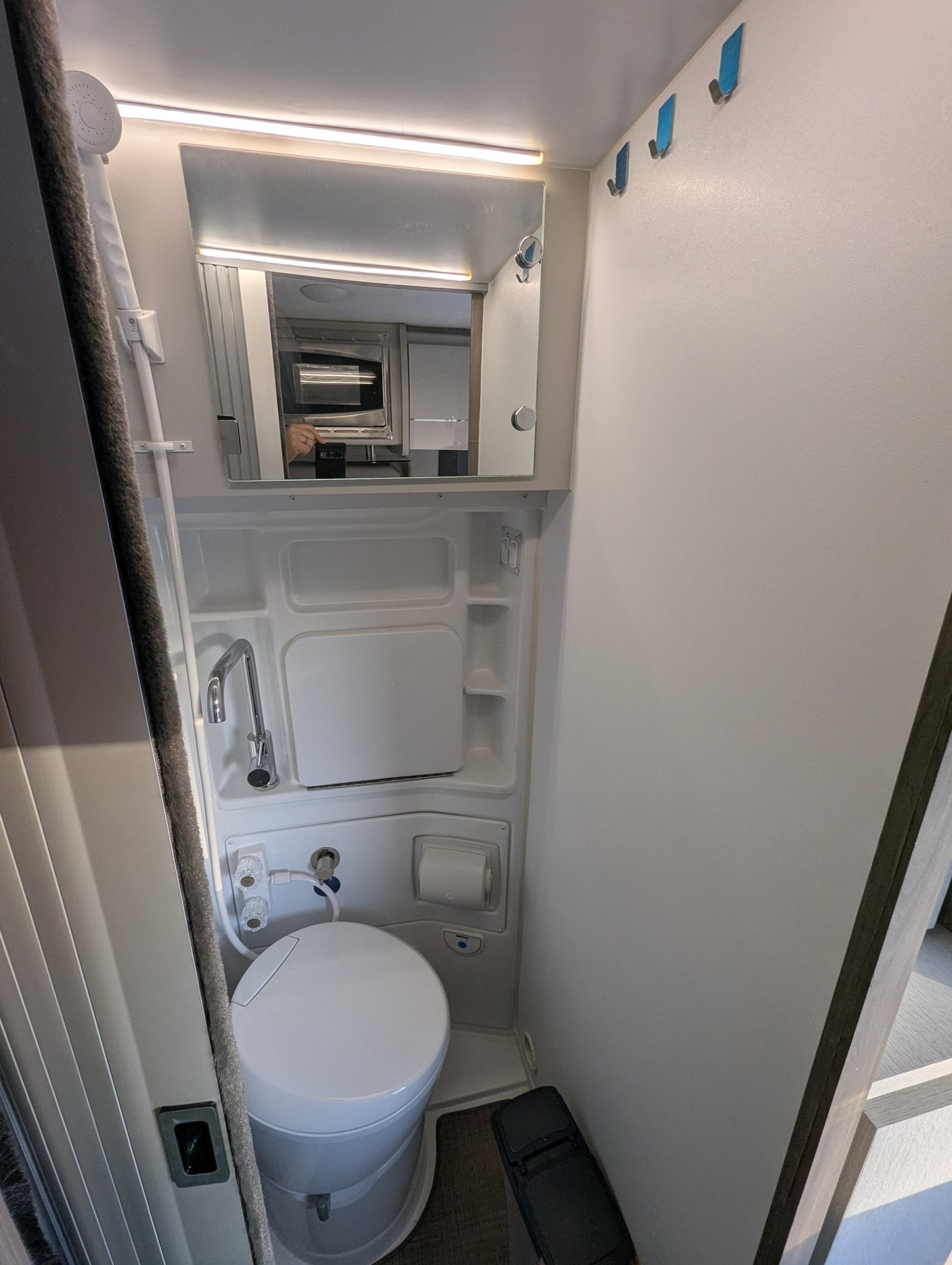 Compact RV rental's wet bath: toilet, shower, sink, mirror reflecting microwave, hooks, and step stool included.