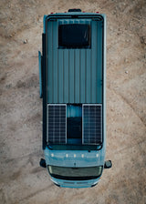Top-down view of a grey Tommy **rv rental** camper van on dirt, with rooftop solar panels & deck. Ready for adventure!