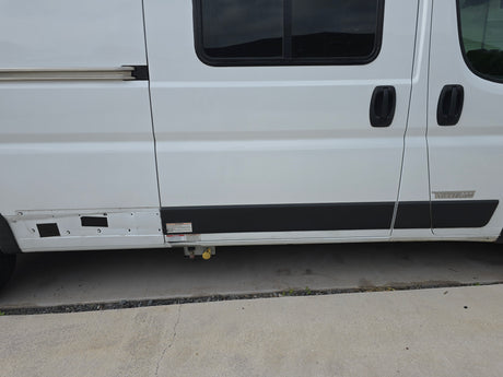Side view of a white Winnebago RV rental, showing sliding door, windows, and external utility connections.