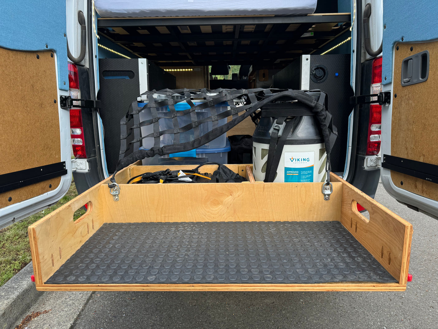 RV rental: Pull-out storage drawer, netted bins, and propane tank optimize space in this van conversion.