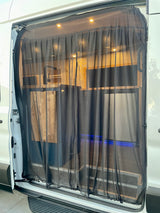 Interior view of an RV rental camper van with a closed magnetic mesh screen door, revealing a functional kitchen and warm lighting.