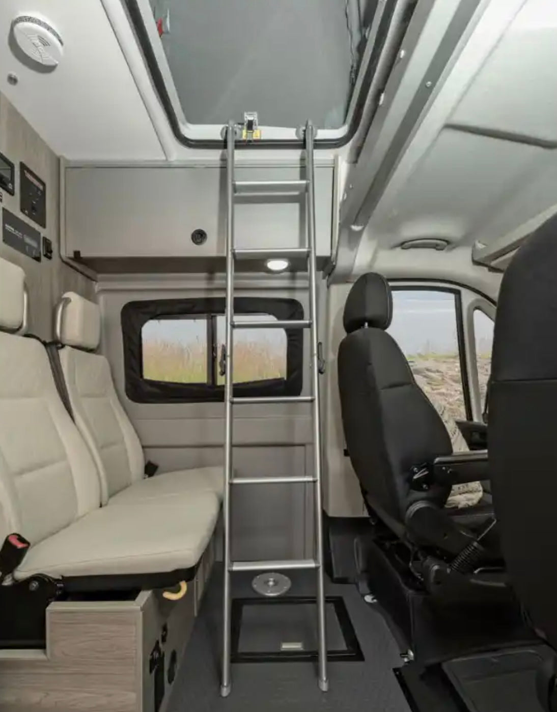 RV rental: Inside a camper van showing a ladder to an upper bunk, ceiling skylight, and passenger seating.