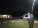 White "Essentials" RV rental van parked in a lit lot at night next to a white building.