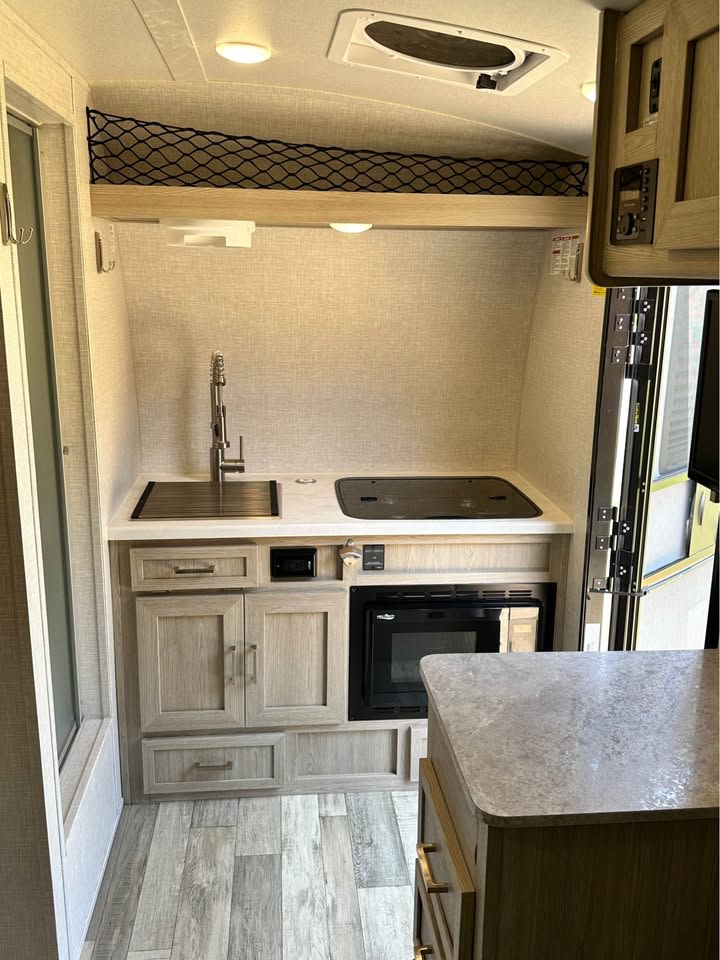 RV rental: A modern, compact kitchen interior featuring a sink, two-burner stove, microwave, and overhead net storage. — photo 3