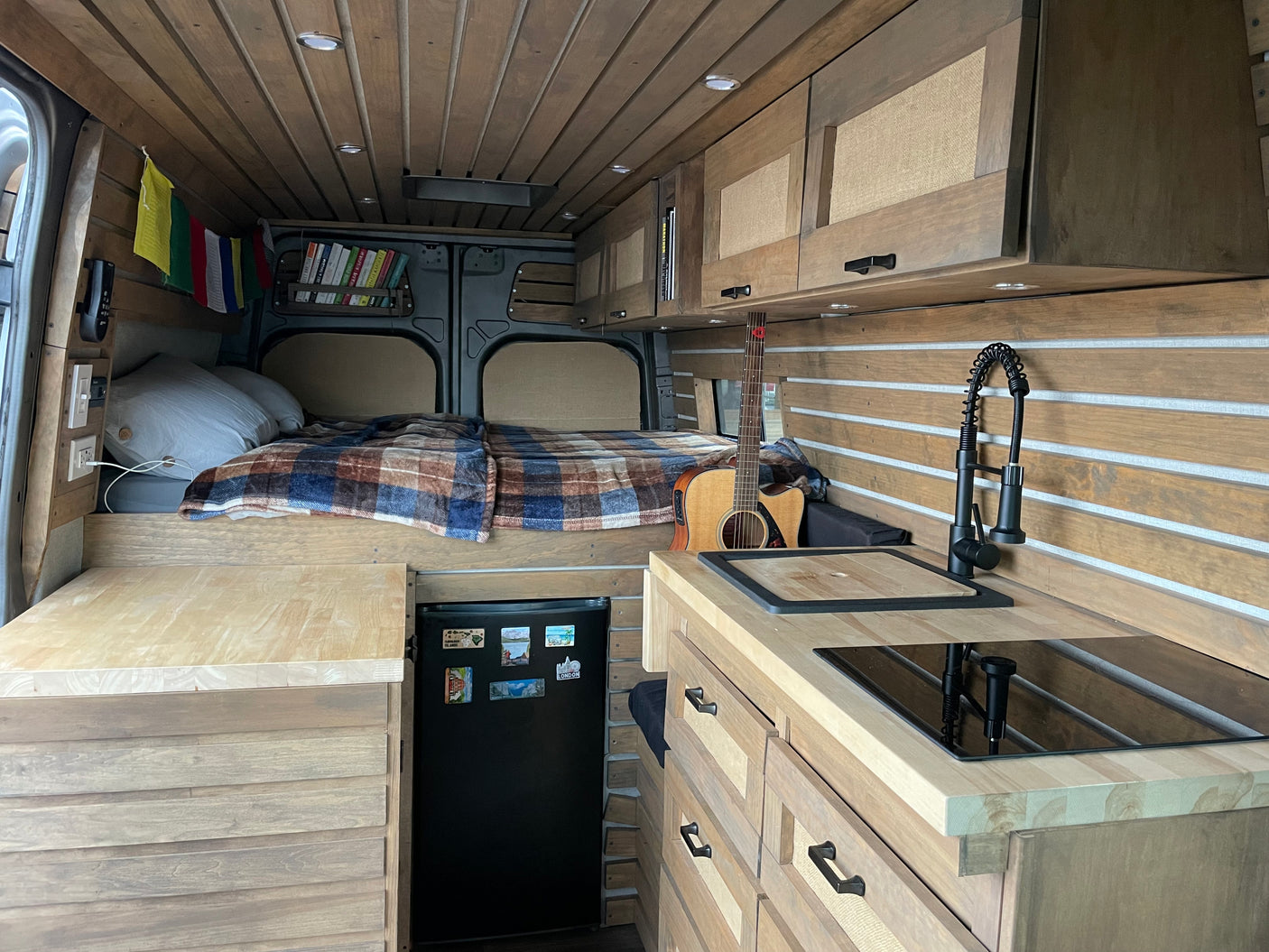 Inside this modern RV rental, find a bespoke wooden interior with a compact kitchen, comfortable bed, and storage solutions.
