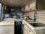 Inside this modern RV rental, find a bespoke wooden interior with a compact kitchen, comfortable bed, and storage solutions.