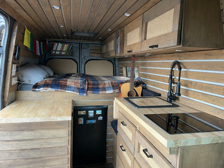 Inside this modern RV rental, find a bespoke wooden interior with a compact kitchen, comfortable bed, and storage solutions.