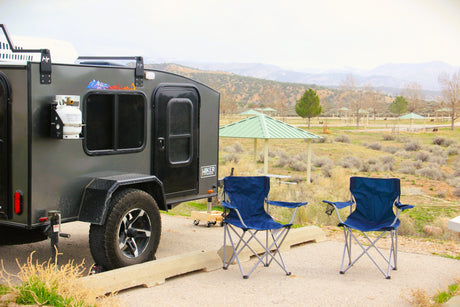 Explore nature with this compact RV rental. Teardrop trailer and camping chairs at a scenic park campsite.