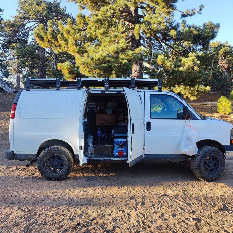 White camper van parked in a pine forest with open side door. See inside this RV rental ready for adventure! — photo 4
