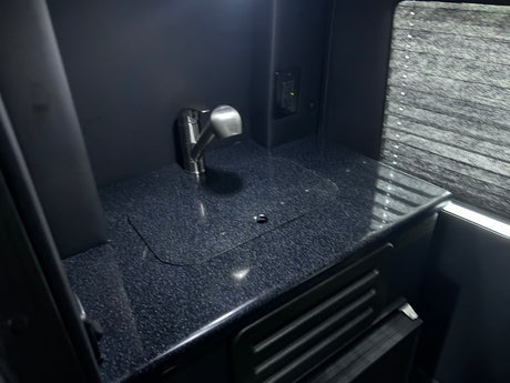 Compact rv rental kitchenette with a modern faucet, dark speckled counter, and window blinds. Ideal for travel.