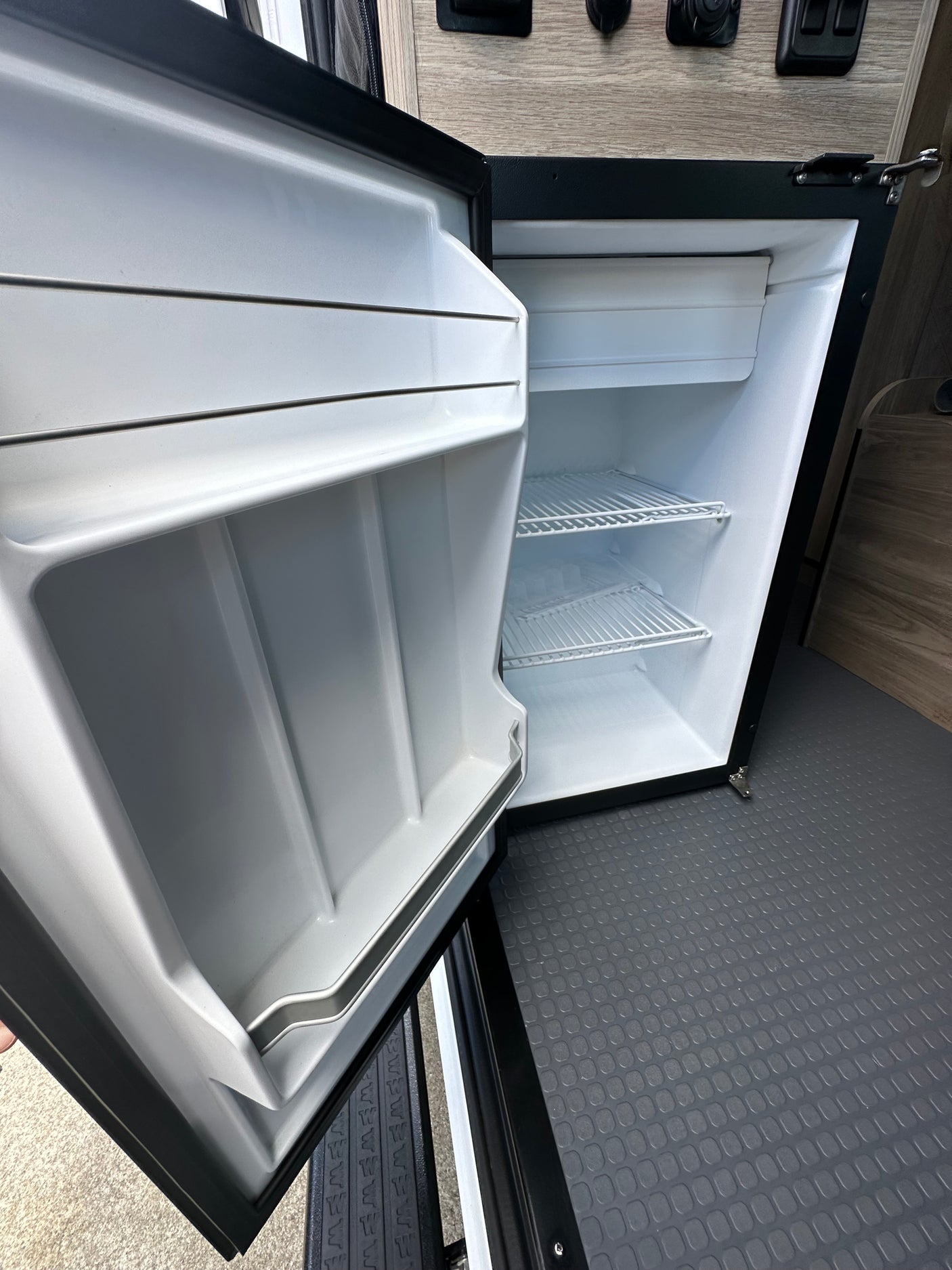 Clean, empty mini-fridge in an RV rental, ready for your adventures. Features wire shelves and a spacious interior.