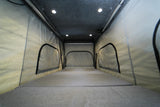 Pop-top sleeping area of an RV rental with comfortable gray mattress, fabric walls, arched windows, and bright lighting.
