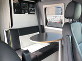 RV rental interior: black and white dining bench, round table, window, and wall-mounted control panel.