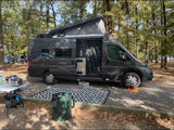 Spacious dark gray rv rental camper van with pop-top set up at a leafy campground. Perfect for outdoor adventure.
