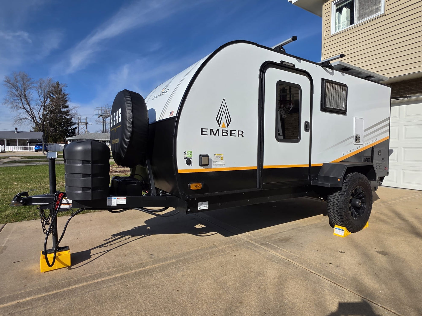 A sleek Ember travel trailer, ideal for an RV rental adventure, is parked. This white and black unit has leveling blocks under its wheels. — photo 8