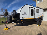 A sleek Ember travel trailer, ideal for an RV rental adventure, is parked. This white and black unit has leveling blocks under its wheels.