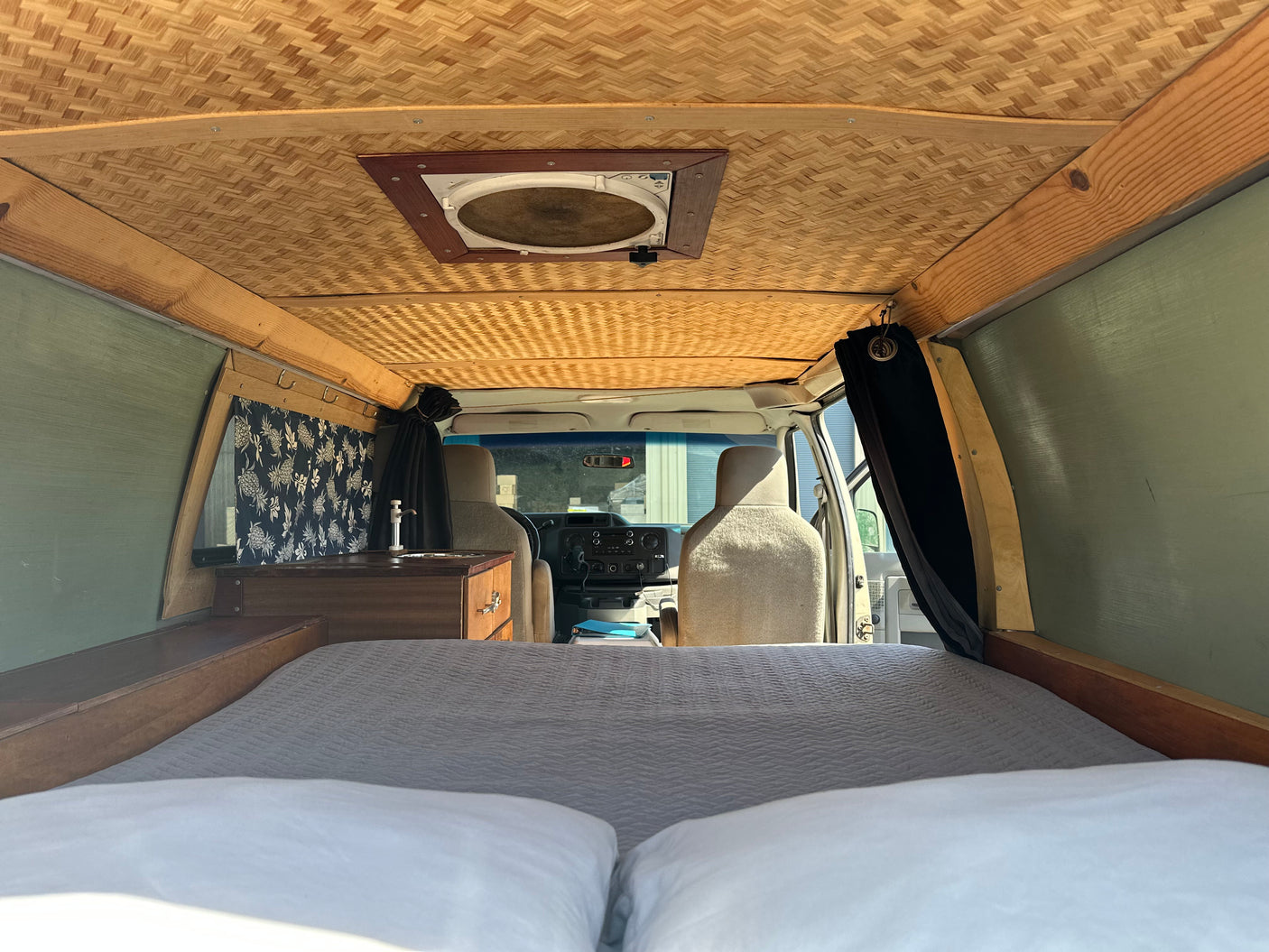 Cozy RV rental interior with bed, kitchen, and bamboo ceiling, perfect for van life adventures and comfortable travel.