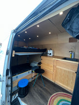 Bright RV rental camper van interior: bunk bed, kitchenette with sink, wood cabinets, smart storage, and cozy lighting. Ready for adventure!