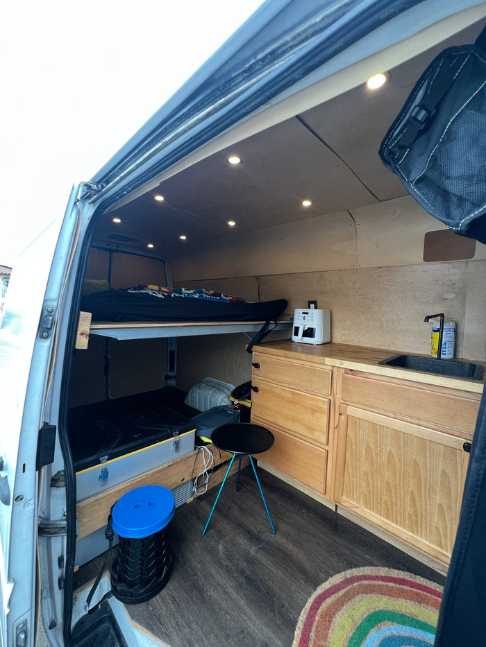 Bright RV rental camper van interior: bunk bed, kitchenette with sink, wood cabinets, smart storage, and cozy lighting. Ready for adventure!