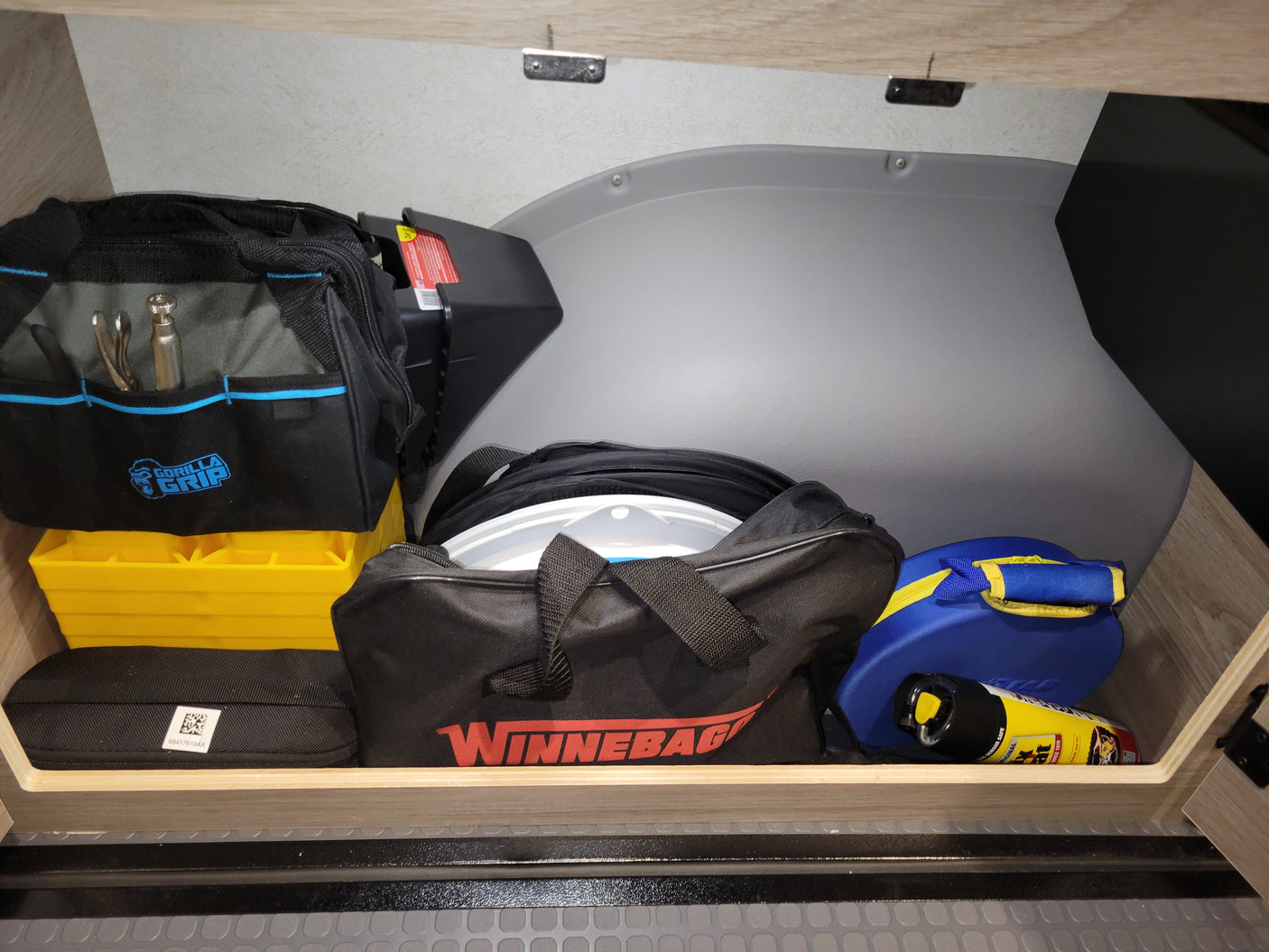 RV rental storage with tools, leveling blocks, Winnebago gear, and emergency tire sealant for safe travels.