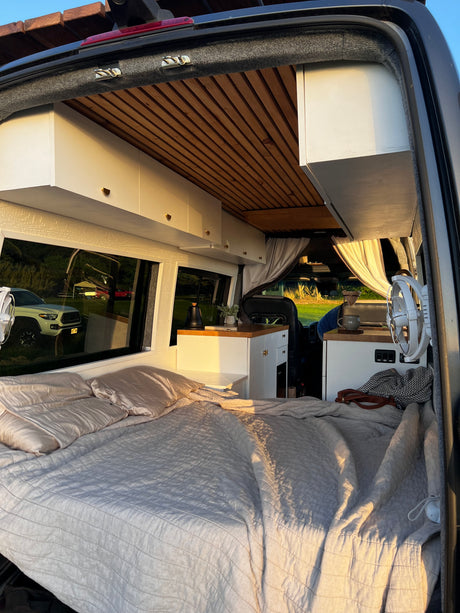 Inside a cozy RV rental: a comfortable bed, natural wood ceiling, and compact kitchen area with natural light.
