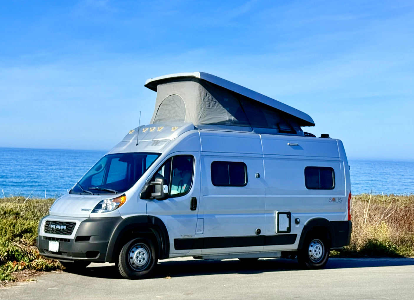 Silver camper van RV rental with pop-top tent, ideal for scenic oceanfront travel & camping.