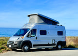 Silver camper van RV rental with pop-top tent, ideal for scenic oceanfront travel & camping.
