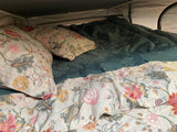 Cozy RV rental bed with vibrant floral pillows & a soft teal comforter, perfect for comfortable glamping on your next road trip.