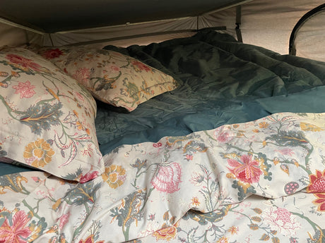 Cozy RV rental bed with vibrant floral pillows & a soft teal comforter, perfect for comfortable glamping on your next road trip.