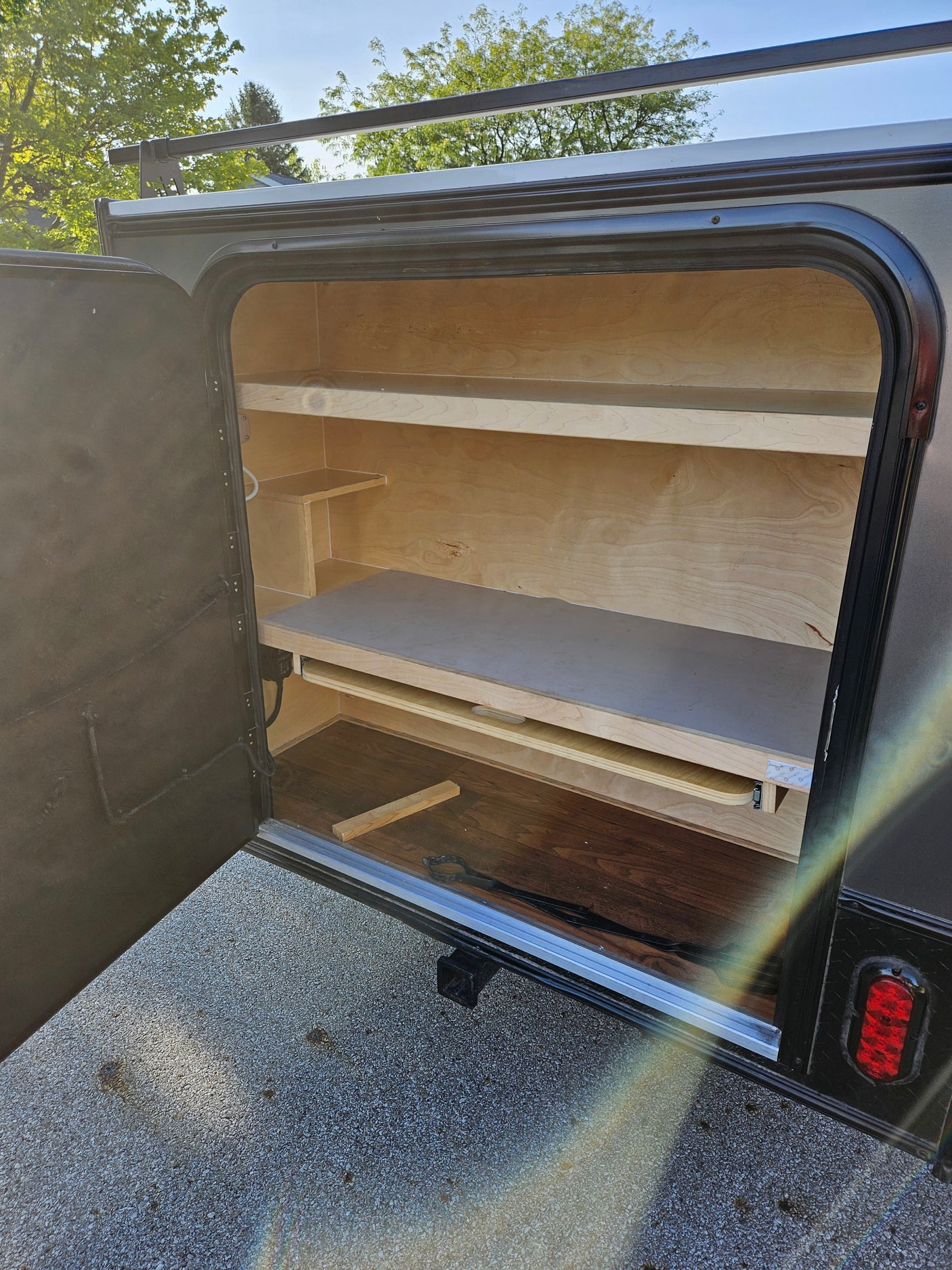 View of an open rv rental storage compartment, featuring wooden shelves and a pull-out drawer for organized travel.
