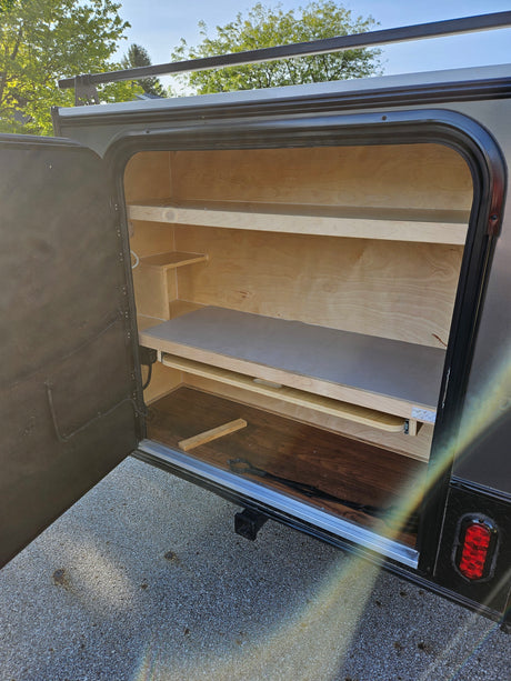 View of an open rv rental storage compartment, featuring wooden shelves and a pull-out drawer for organized travel.