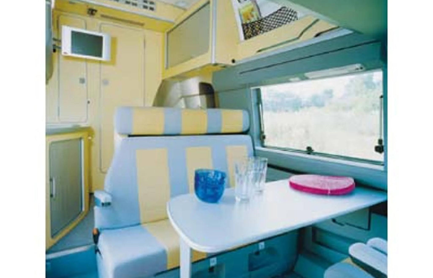This rv rental features a compact dining area with a table, patterned seating, and a mounted TV, showcasing a bright interior.