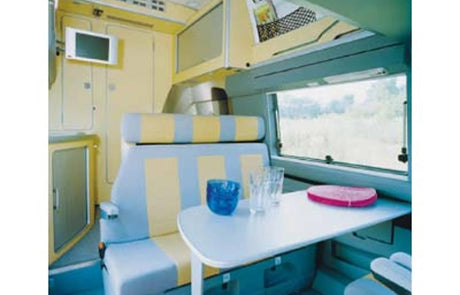 This rv rental features a compact dining area with a table, patterned seating, and a mounted TV, showcasing a bright interior.