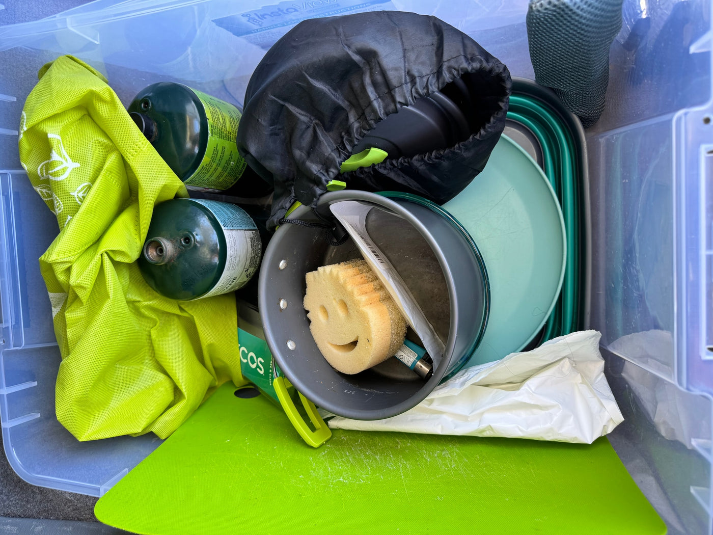 Packed RV rental camping supplies: propane tanks, cookware, collapsible dishes, and a smiley sponge in a clear tote. — photo 10