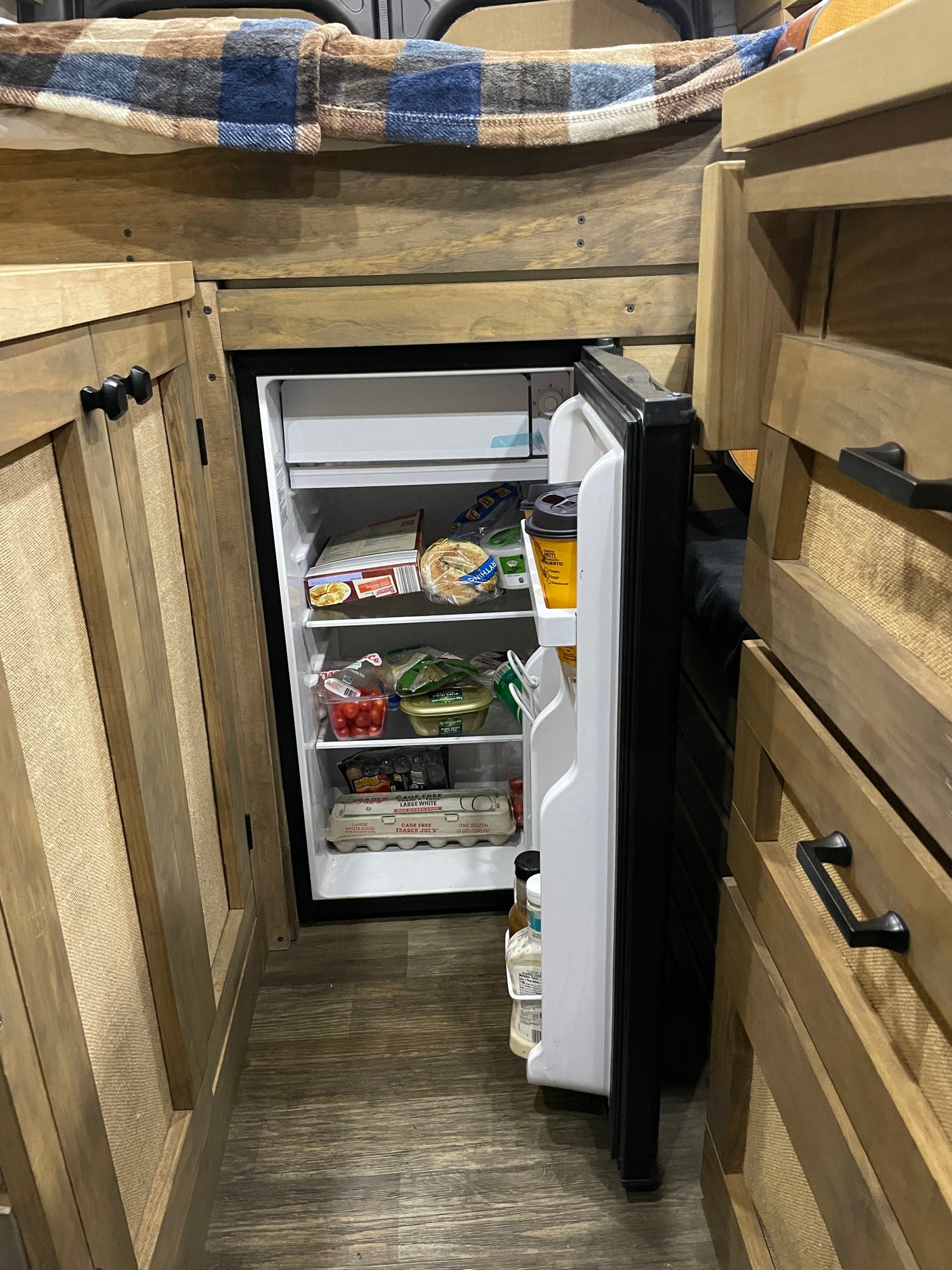 Stocked compact refrigerator in an RV rental, showing the kitchen area and cozy wooden interior.