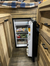 Stocked compact refrigerator in an RV rental, showing the kitchen area and cozy wooden interior.