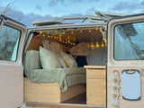 Interior of a cozy, custom-built camper van, showing a bed with pillows, string lights, and storage. Ideal for rv rental.