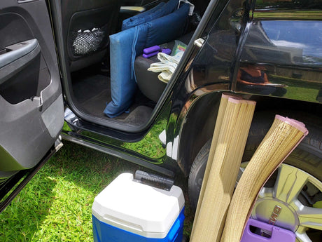 Car packing for RV rental trip: blue cushions, cooler, and rolled mats.