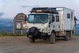 Front three-quarter view of the 2021 Isuzu NPR Crew Cab 4x4 expedition rig at a trailhead
