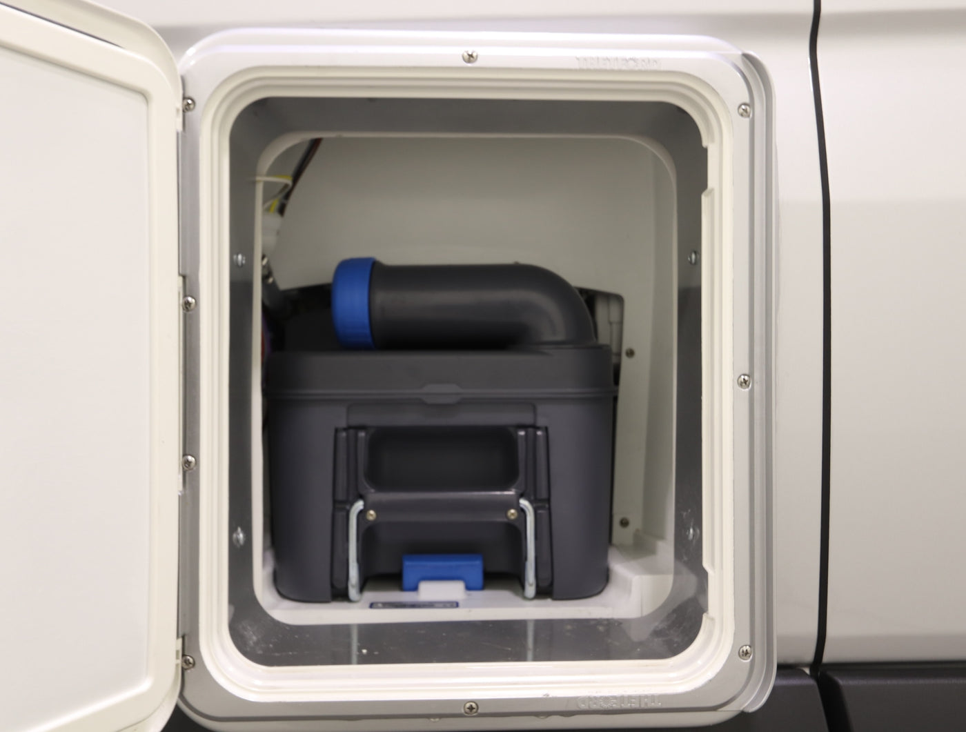 RV rental external compartment showing a dark gray cassette toilet waste tank with a blue cap. Essential for camper sanitation. — photo 15