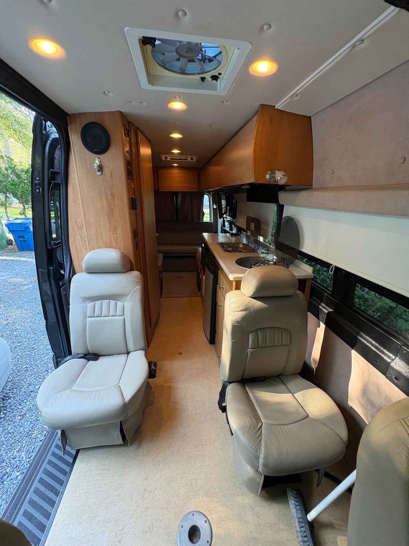 View inside an RV rental showing front swivel seats, a compact kitchenette with sink/stove, overhead cabinets, and rear living area.