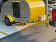 Compact yellow & gray teardrop RV rental trailer hitched to a truck