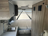 RV rental interior featuring a convertible bed, compact kitchen with sink, and overhead storage. Ideal for travel.