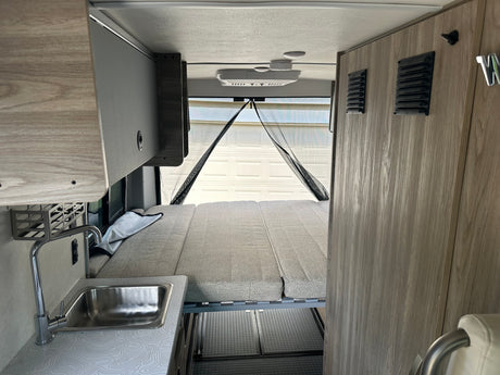 RV rental interior featuring a convertible bed, compact kitchen with sink, and overhead storage. Ideal for travel.