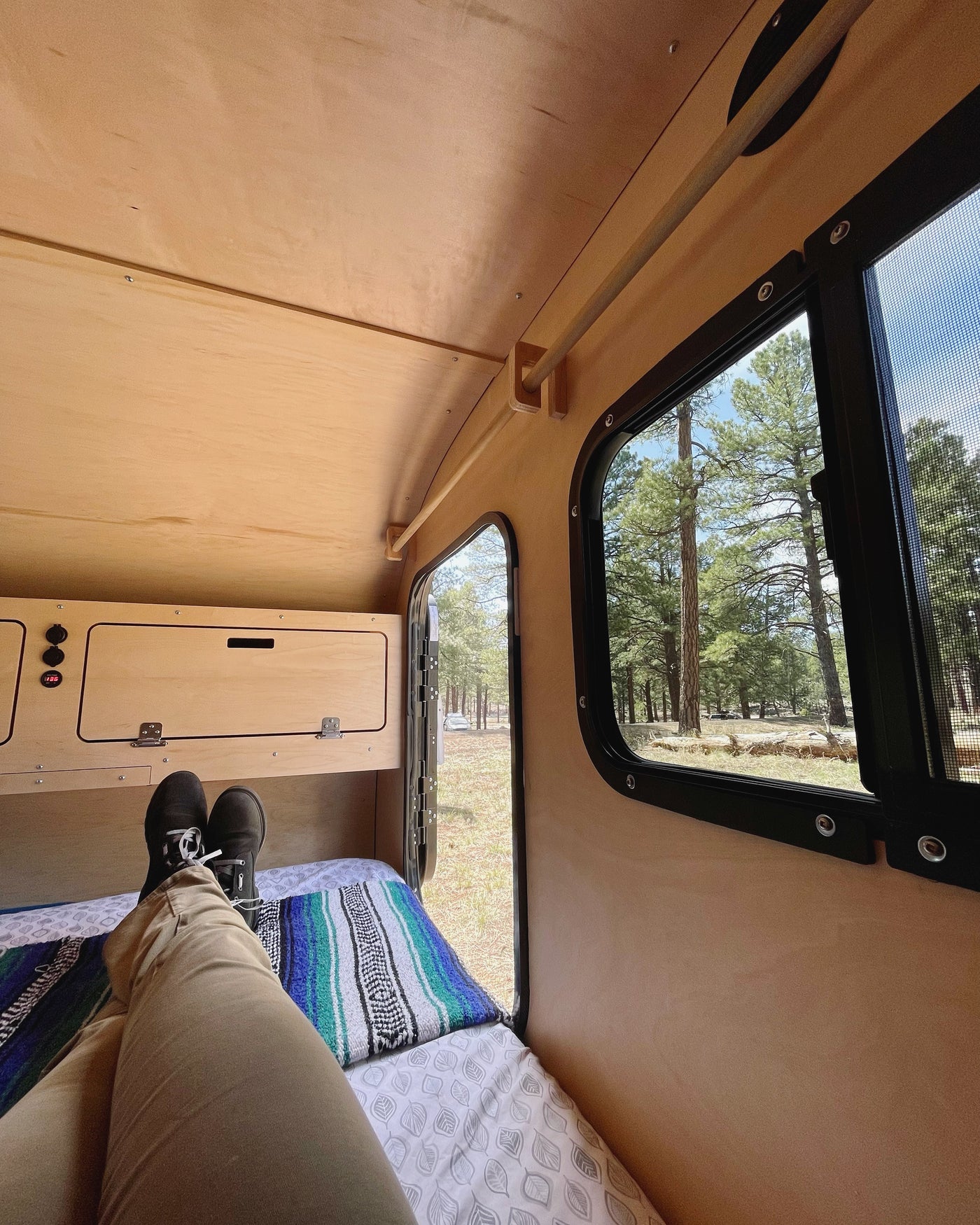 Feet up, relaxing inside a compact rv rental. Enjoying the forest view through the window and open door on a bed. — photo 16