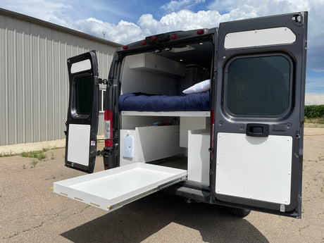 Discover the rear of this RV rental camper van with open doors, revealing a comfortable bed, under-bed storage, and an extended pull-out tray.