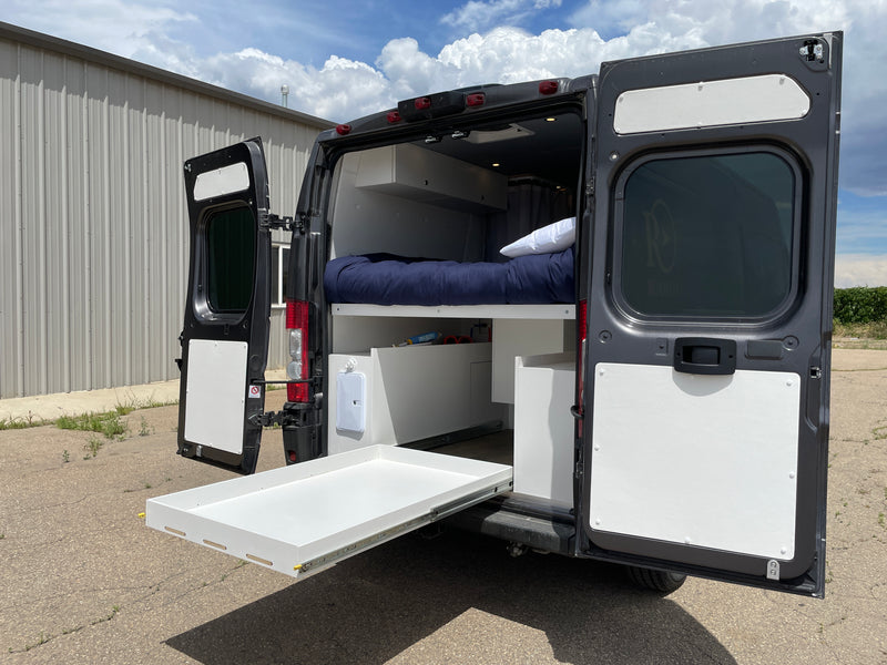 Discover the rear of this RV rental camper van with open doors, revealing a comfortable bed, under-bed storage, and an extended pull-out tray. — photo 8