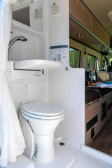 Efficient RV rental bathroom featuring a toilet, integrated pull-out sink/shower, and privacy curtain. Perfect for camper van travel.